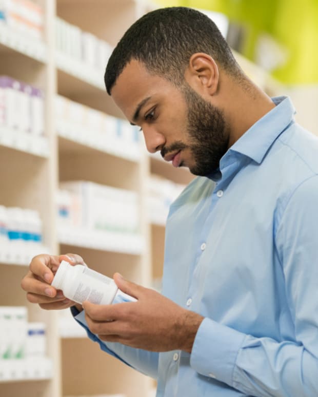 A man in a blue shirt holding a bottle of probiotic supplements as he stands in front of a shelf full of similar products